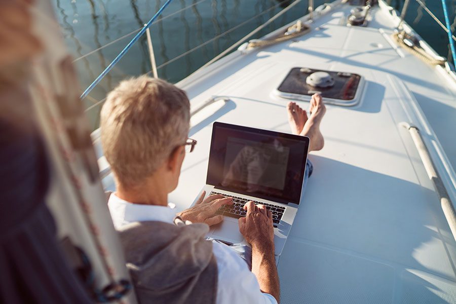 Insurance Quote - View of Mature Man Sitting on a Sailboat Using a Laptop